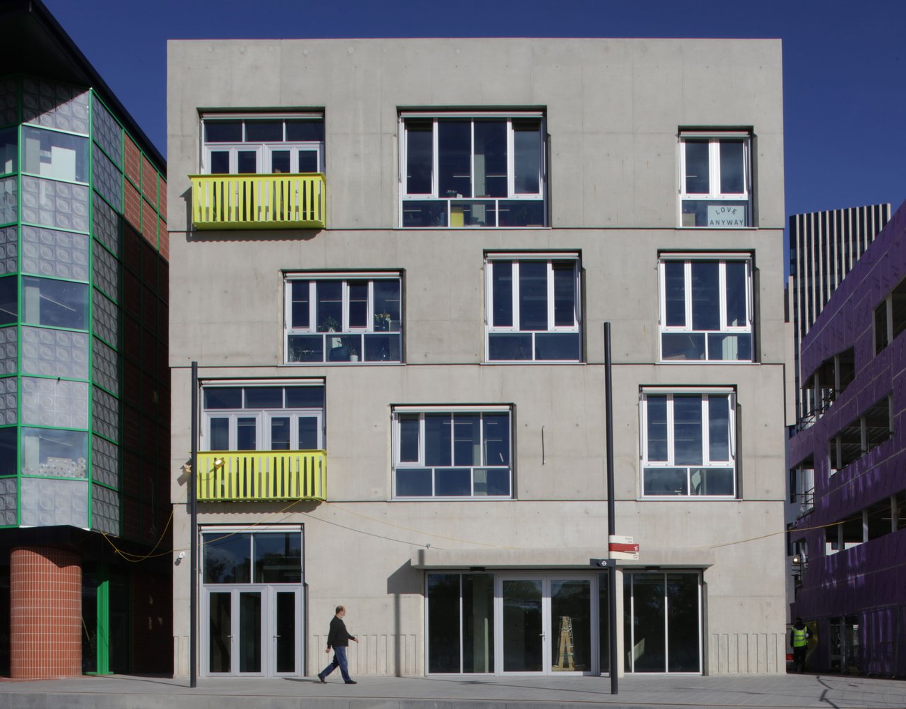 Upward view of a concrete building corner with large windows and projecting awnings against the sky